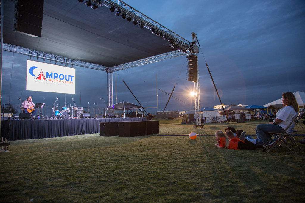 People sitting on the grass in front of the performance stage at Campout Against Cancer