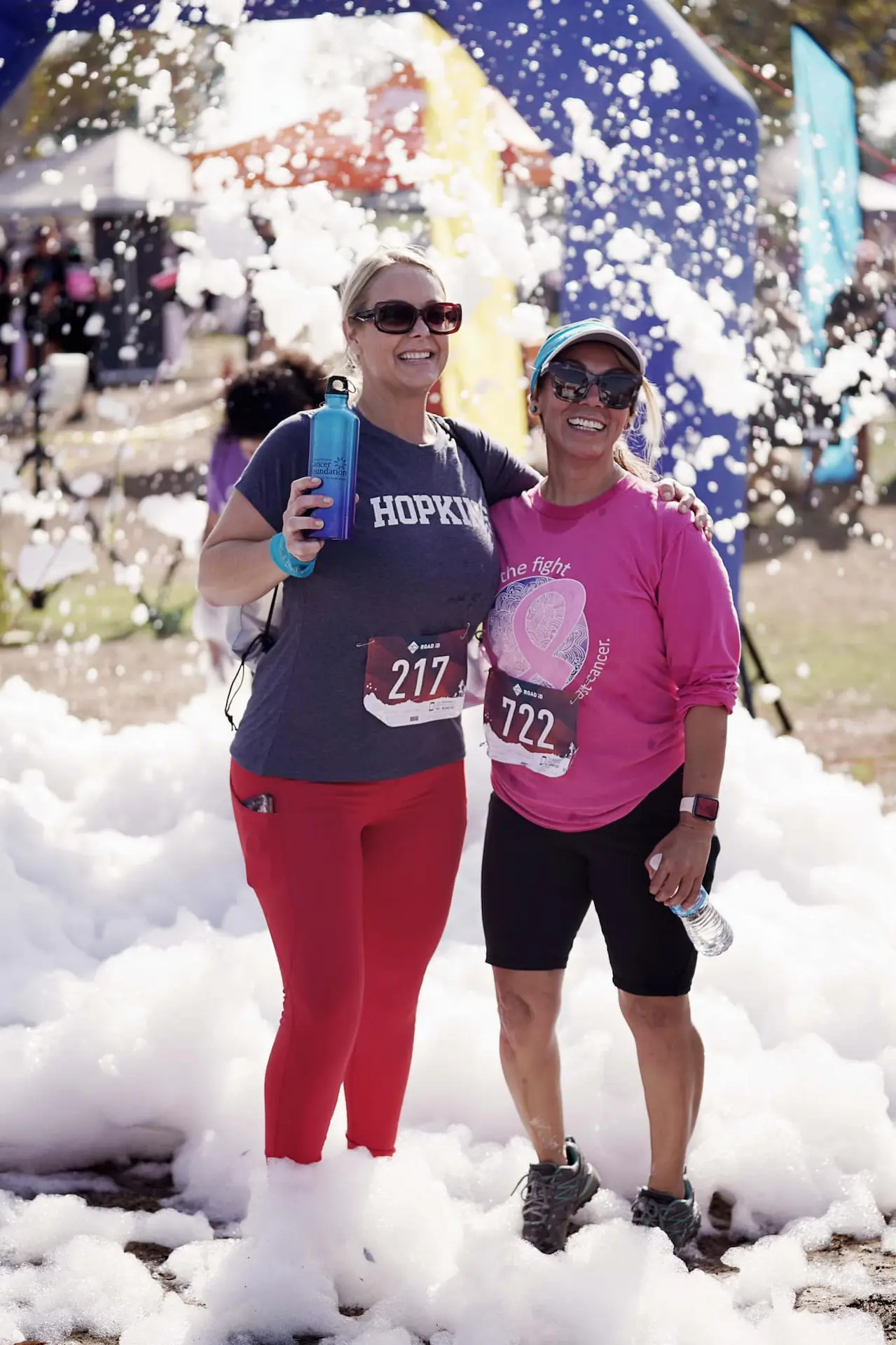 Two women smiling and posing in a pile of foamy bubbles at Kern Run Walk