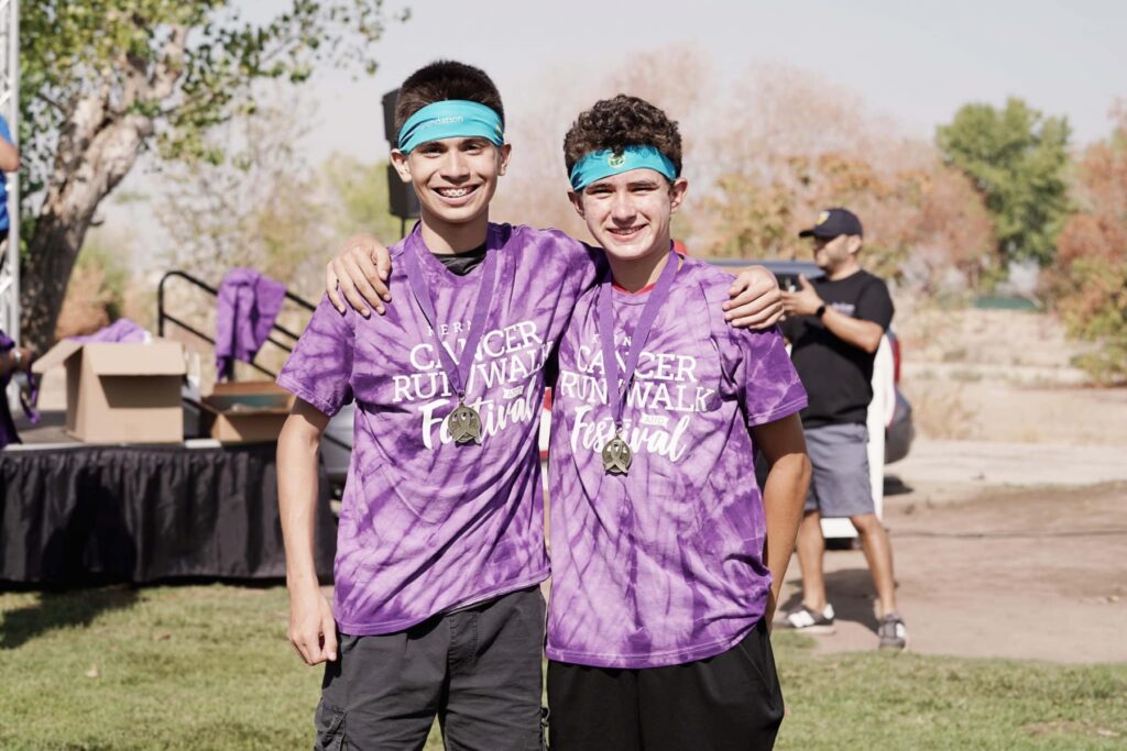 Two adolescents wearing purple tie dye Kern Cancer Run Walk shirts hugging side by side at Kern Run Walk